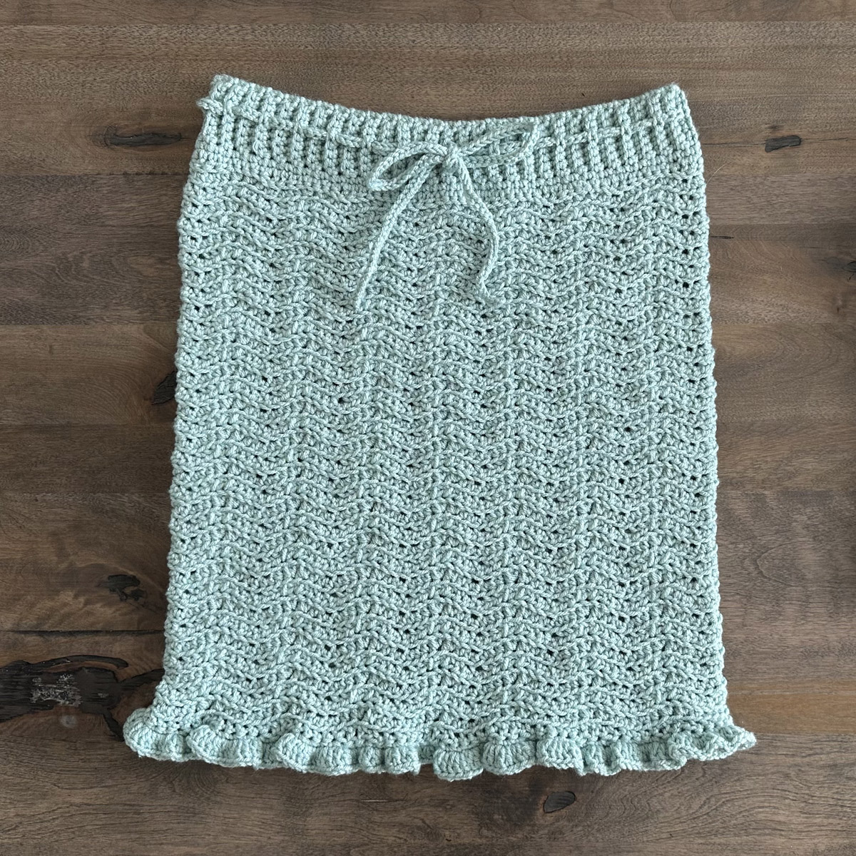 A ripple pattern crocheted pencil skirt in aqua acrylic yarn displayed on a wood background.